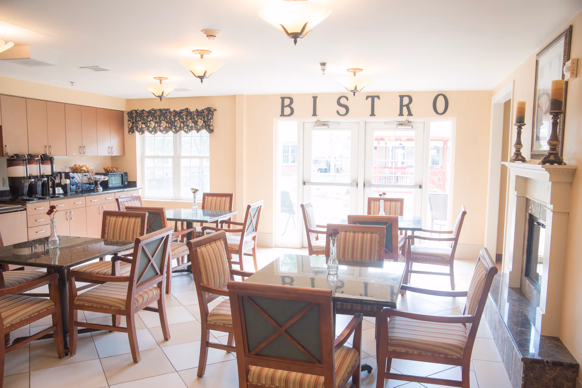 Bright bistro-style dining room with multiple tables and chairs, a serving counter and a fireplace.