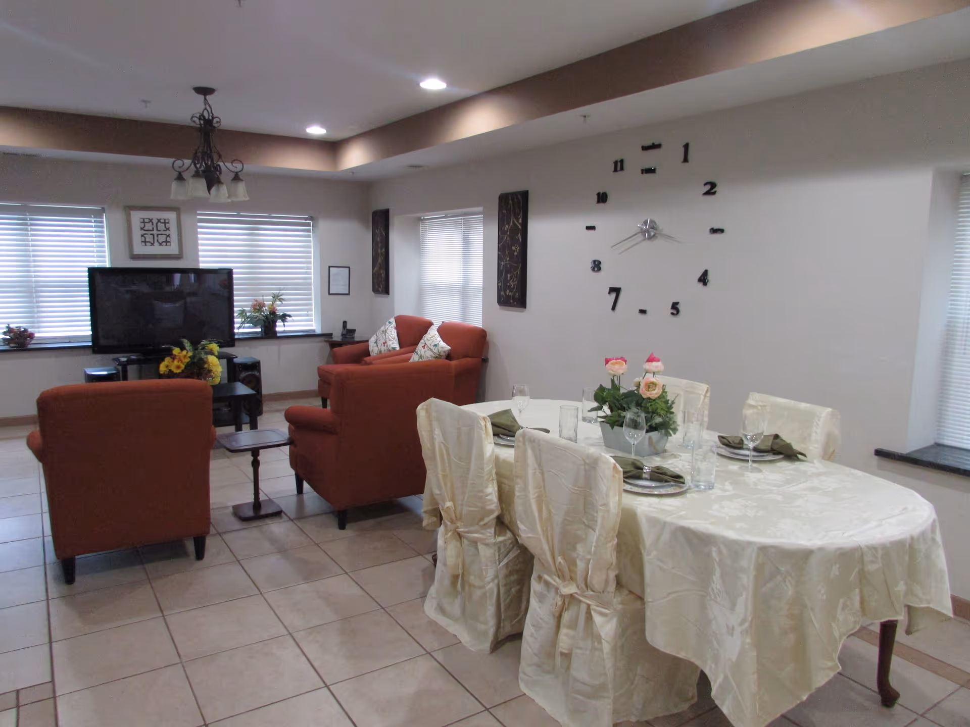 A communal living and dining area with a round table, red armchairs, and a wall clock.