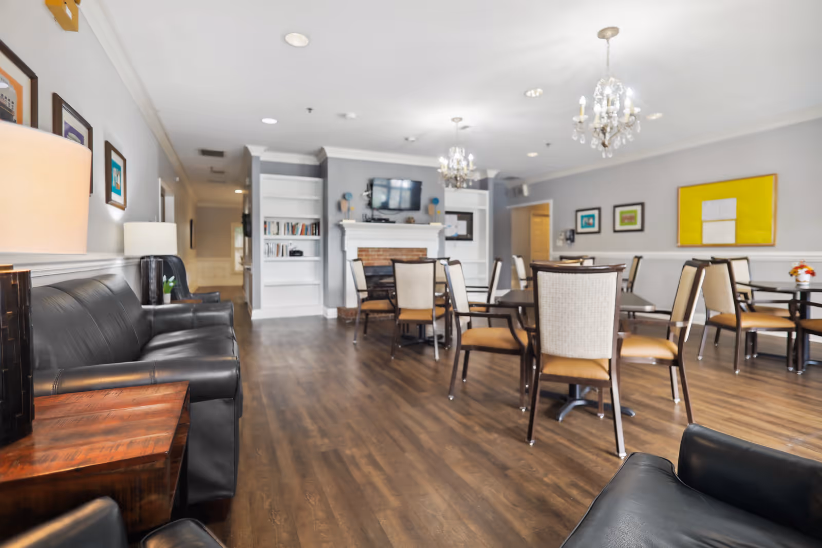 Spacious communal dining and lounge area with tables, chairs, sofas, a fireplace, and chandeliers.