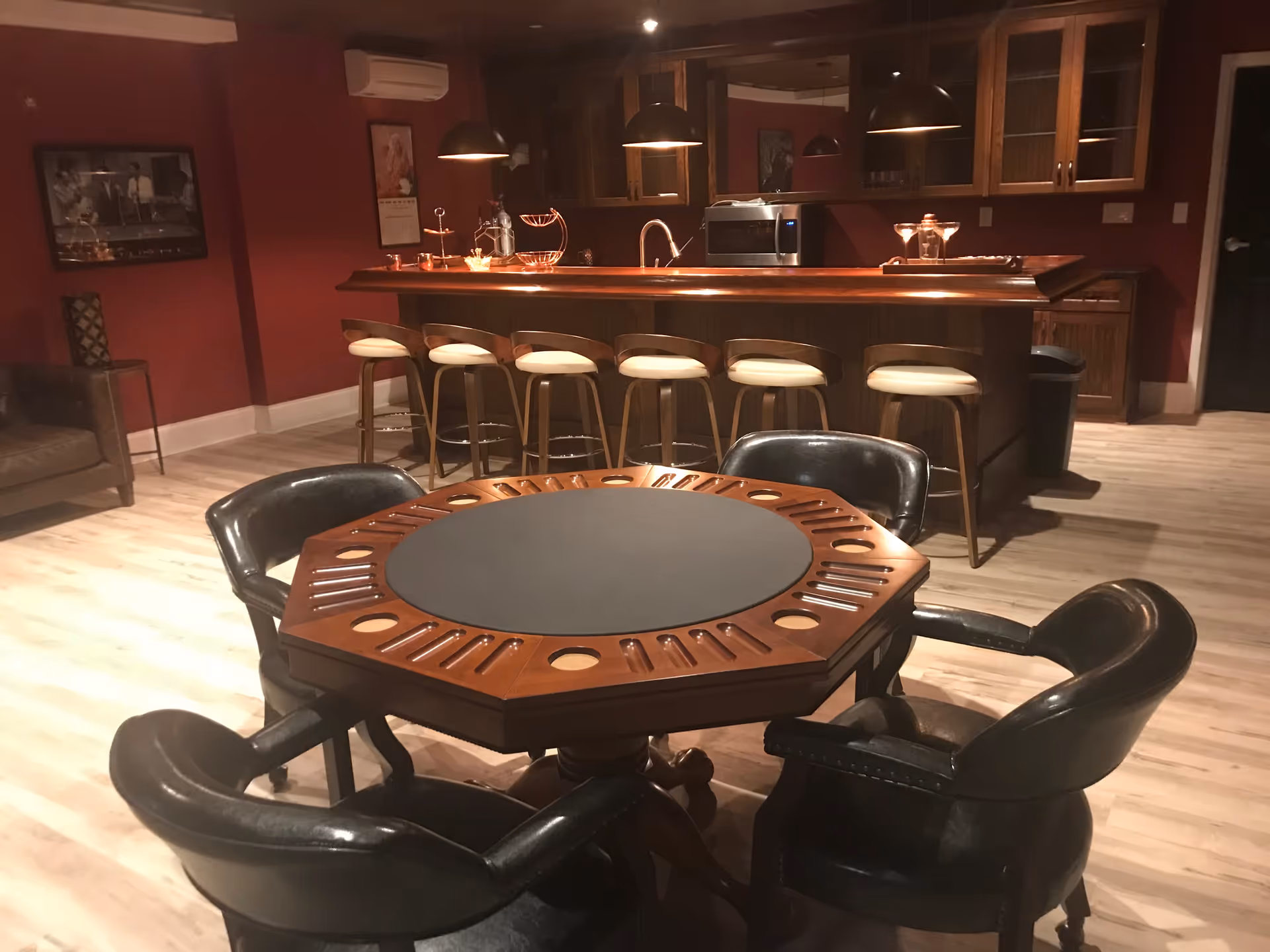 Octagonal card table surrounded by leather chairs in a warmly lit room with a wooden bar and stools.