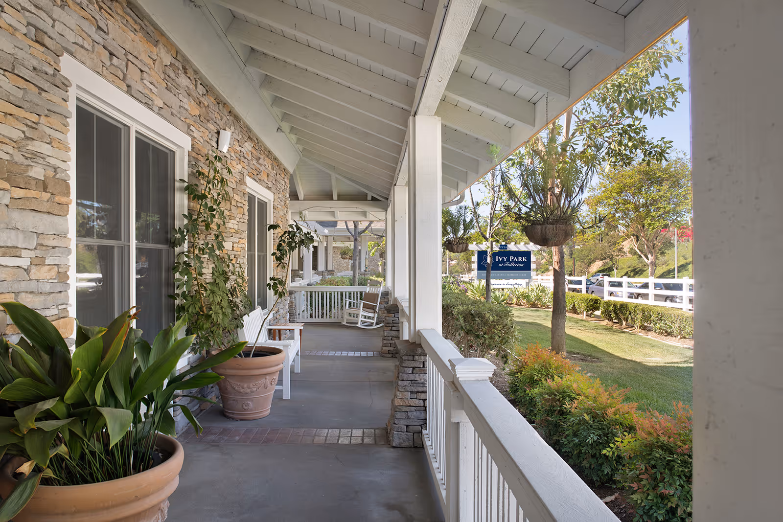 Covered front porch with potted plants, white railings and rocking chairs overlooking a lawn and an Ivy Park sign.