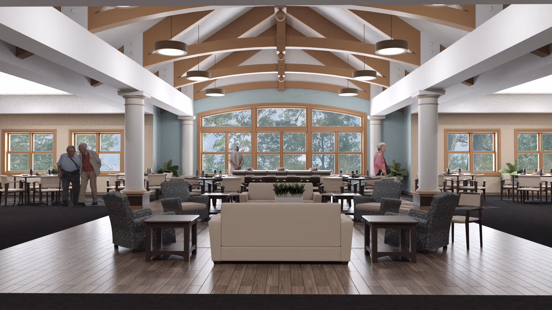 A spacious senior living facility common area with a high vaulted ceiling featuring wooden beams and hanging circular lights. The room includes a seating area with beige sofas and patterned armchairs around wooden side tables on a wooden floor. In the background, there are multiple dining tables and chairs near large windows showing trees outside. Three elderly people are visible: one standing near the windows, one walking, and two conversing near the left side of the room.
