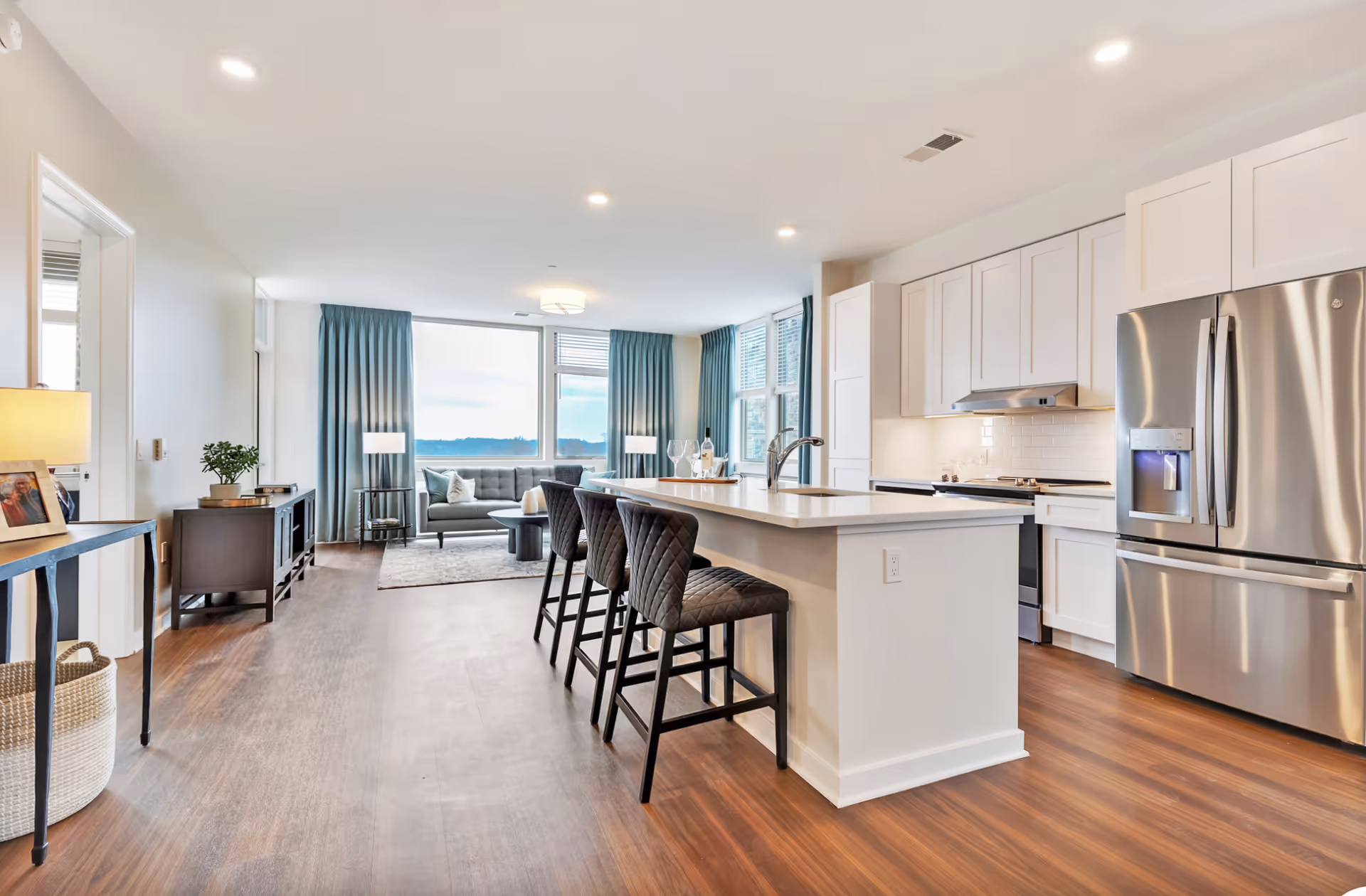 Bright open-plan kitchen with a large island and bar stools opening to a living area with a sofa and large windows.