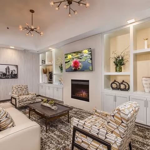 Contemporary lounge with patterned armchairs and a sofa around a coffee table, a wall-mounted TV above a fireplace, and built-in shelving.