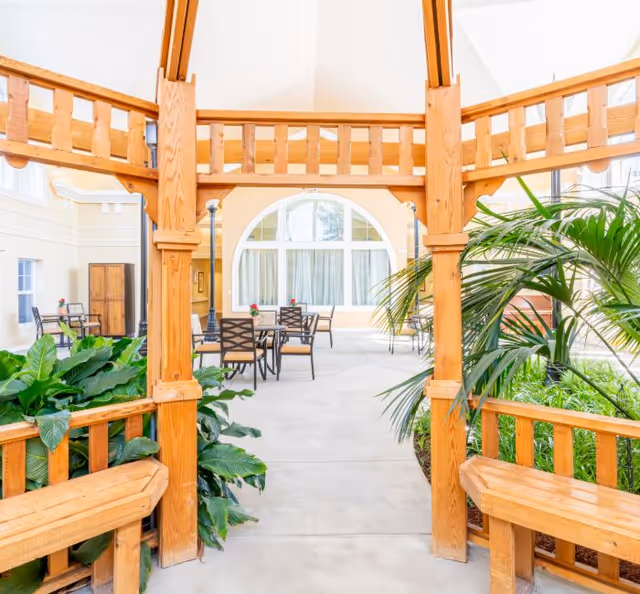 Bright indoor atrium featuring a wooden pergola, lush plants, and tables with chairs.