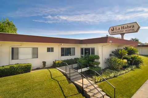 Outside view of La Habra Convalescent Hospital entrance with a manicured lawn and sign.