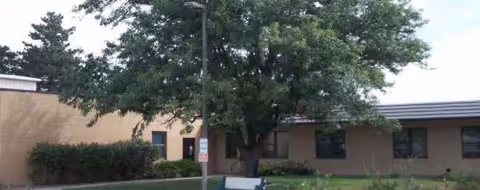 Exterior view of a single-story facility with a tree and windows.