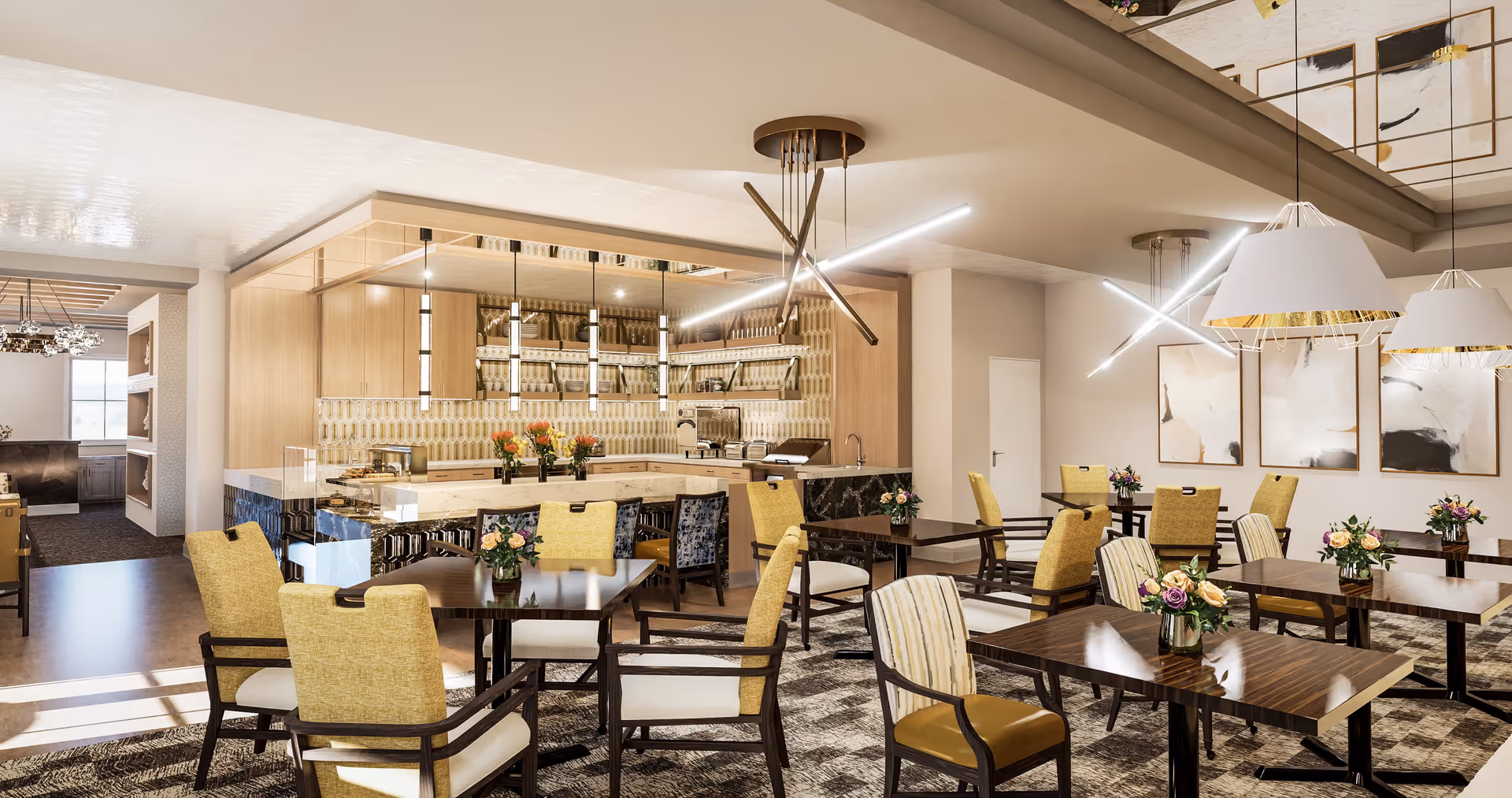 A modern dining room with multiple tables and chairs, some with yellow upholstery and others with striped fabric. Each table has a small floral arrangement. The room features contemporary lighting fixtures hanging from the ceiling and abstract artwork on the walls. In the background, there is a kitchen area with wooden cabinets, a patterned backsplash, and a marble countertop.