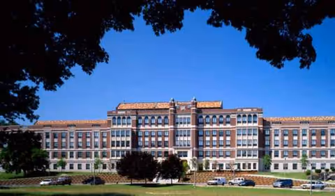 Exterior view of a large brick senior residence building with cars and trees.