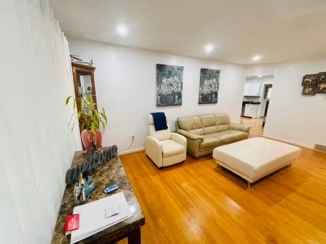 Bright living room with hardwood floors, a beige leather sofa, armchair and ottoman, a console table with decor, and floral wall art.