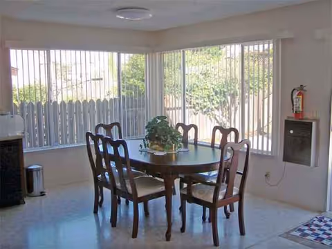 A dining room in a senior care home with a round table and potted plant centerpiece.