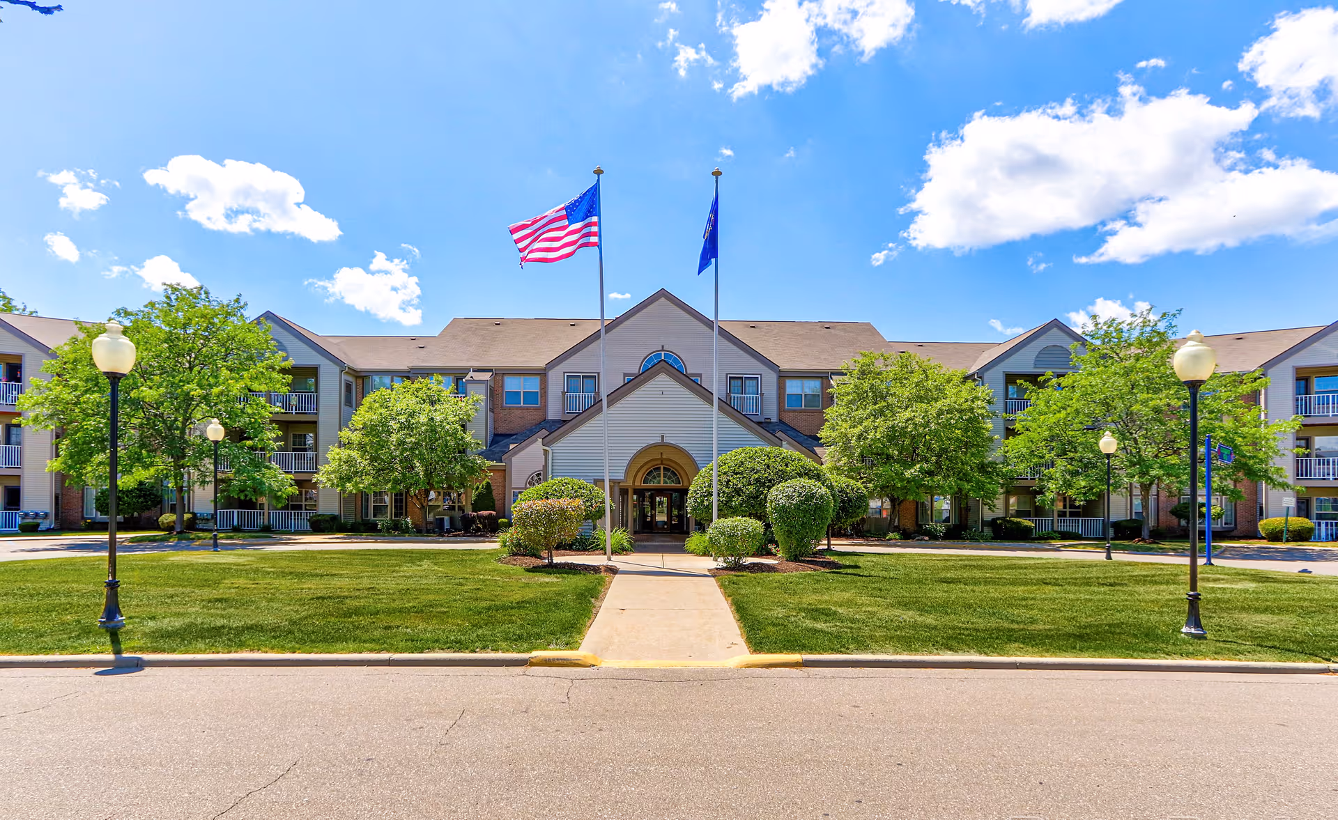 Front exterior of Rosehaven Manor building with two flagpoles, landscaped lawn, and a central walkway leading to the entrance.
