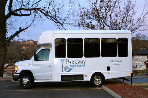 A white Parkway Health & Rehab shuttle bus parked outdoors near trees and houses.