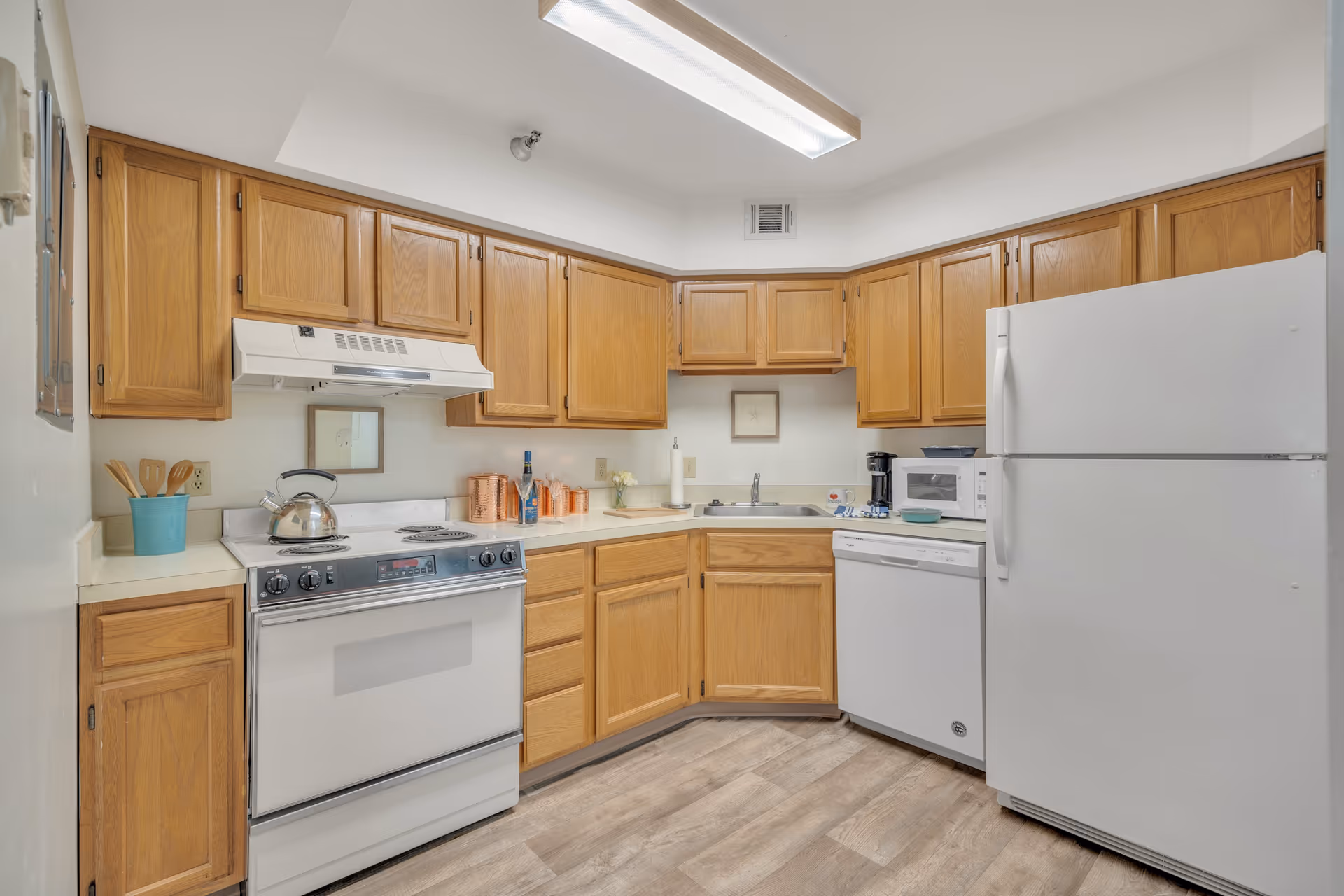 Compact kitchen with oak cabinets and white appliances including a stove, refrigerator, dishwasher, microwave, and sink.