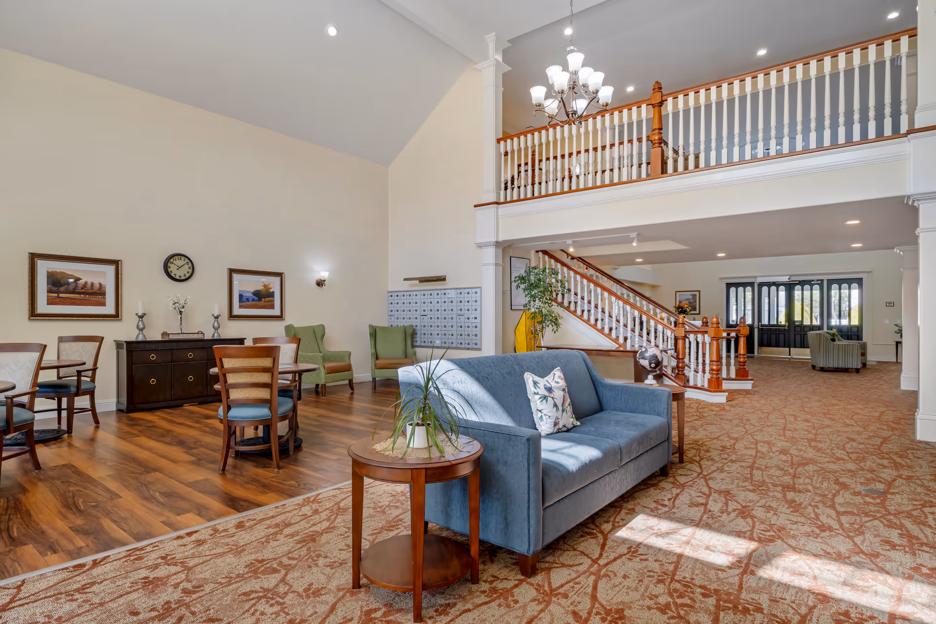 Bright, airy senior living facility lobby with seating, a staircase, and a second-floor balcony.
