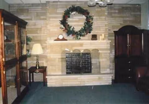 Living room with a stone fireplace, wreath above mantel, and surrounding furniture.