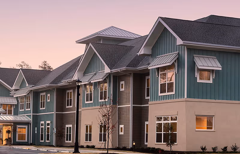 Exterior view of a two-story teal and beige residential building with multiple windows and pitched roofs at dusk.