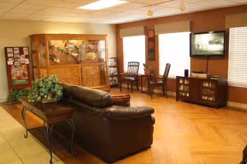 Cozy living room in a senior facility with leather sofa, TV, and wooden furniture.