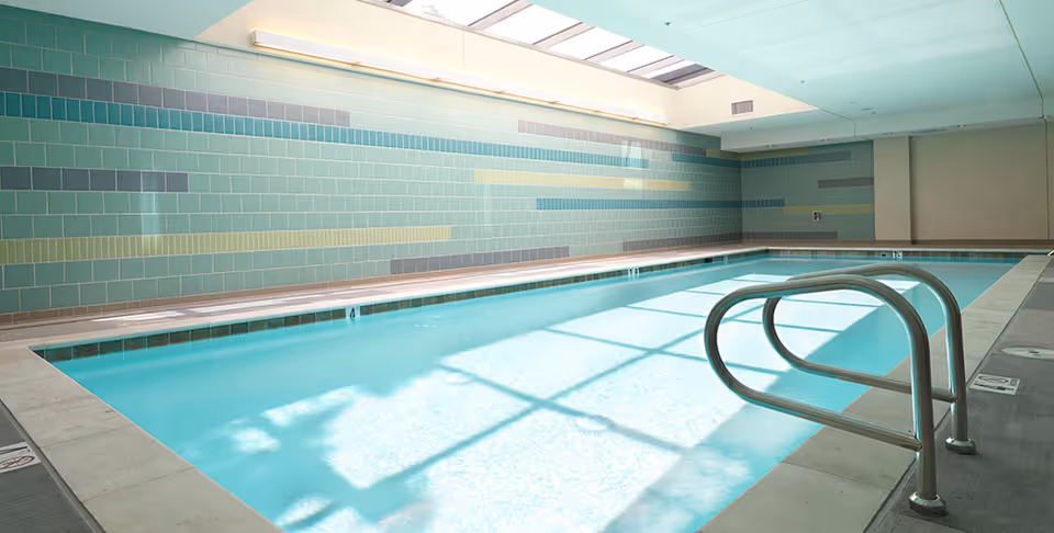 Indoor swimming pool with a metal handrail, tiled walls, and a skylight casting light onto the water.