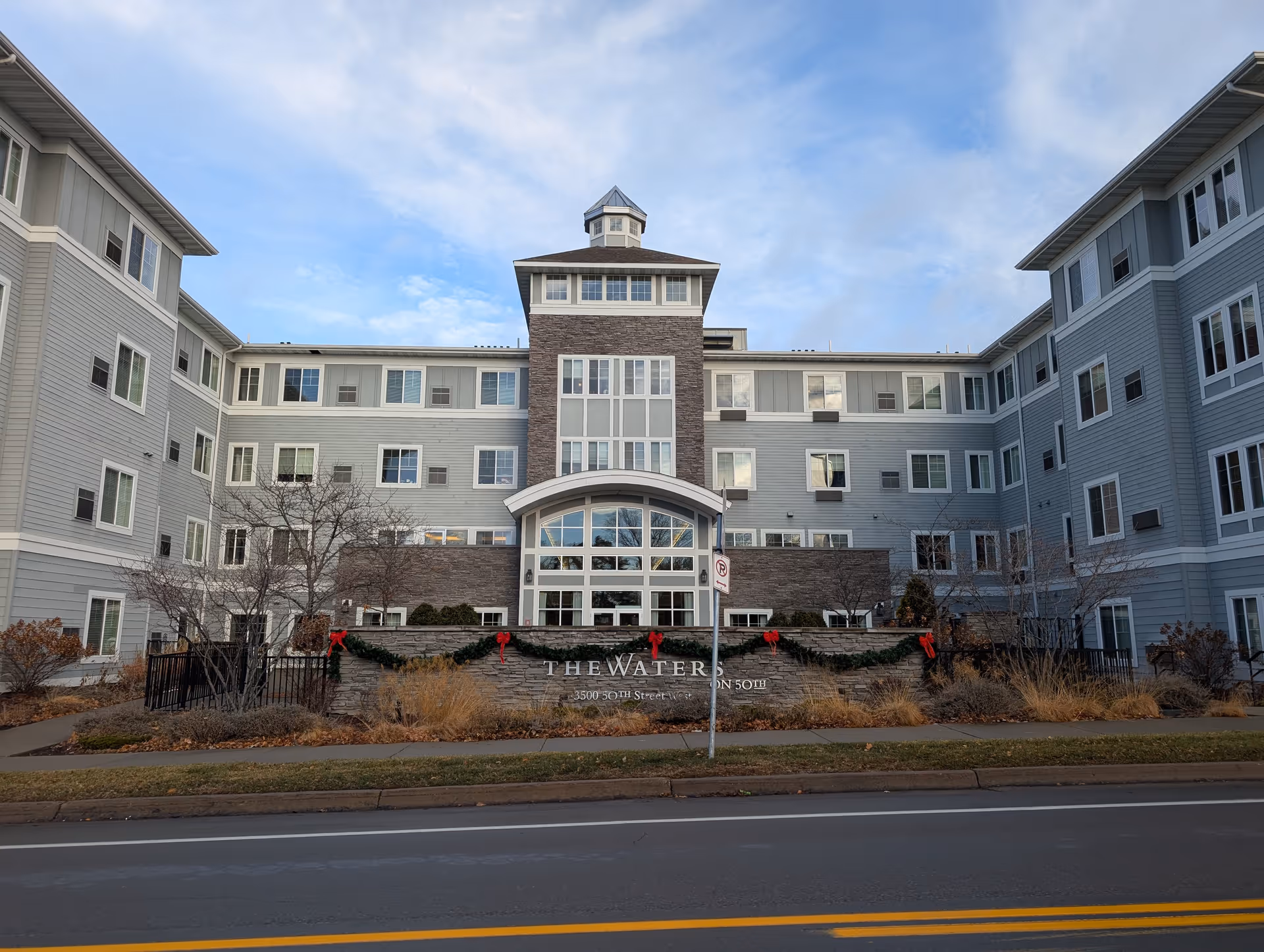 Front exterior of The Waters of Edina senior living building, a multi-story gray facade with a central glass entrance.