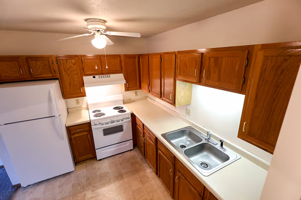 Kitchen with oak cabinets, white refrigerator and electric stove, a double stainless steel sink, and tiled floor.