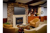 Cozy lounge with a stone fireplace, wall-mounted TV, built-in shelving, and comfortable armchairs around a coffee table.