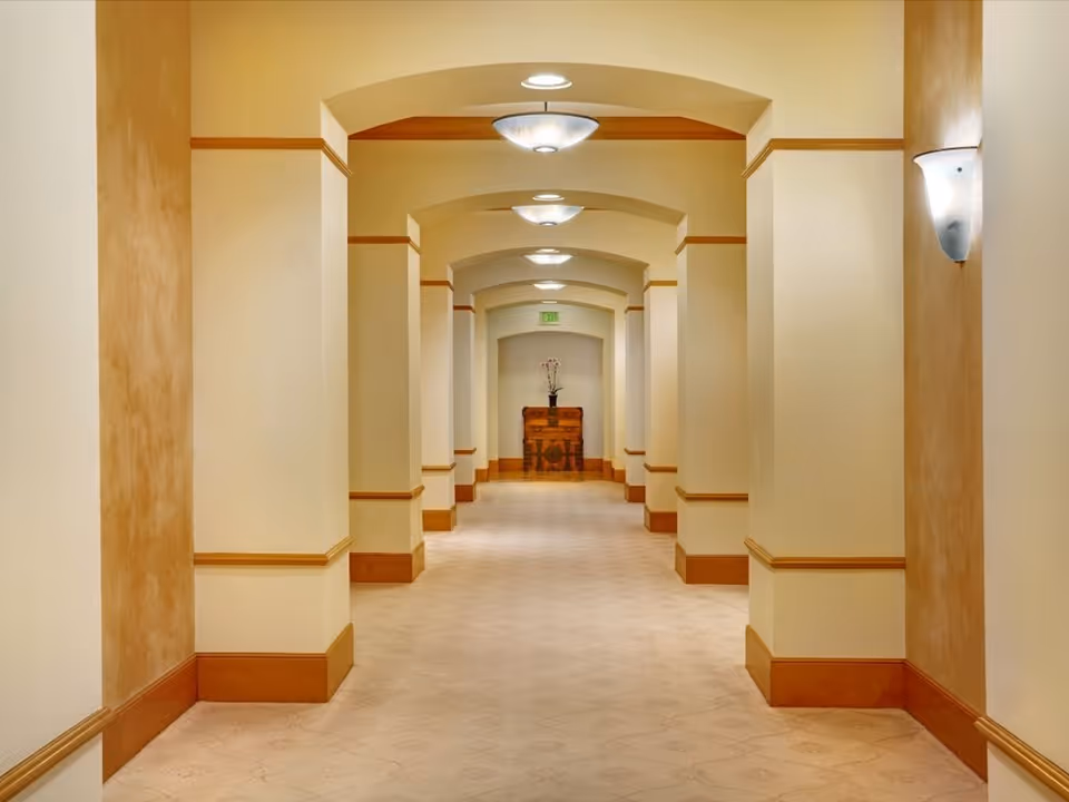 Carpeted hallway with arched ceilings, wall sconces and a decorative chest at the far end.