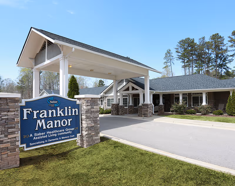 Front view of a senior living facility with a covered entrance and a large blue Franklin Manor sign.