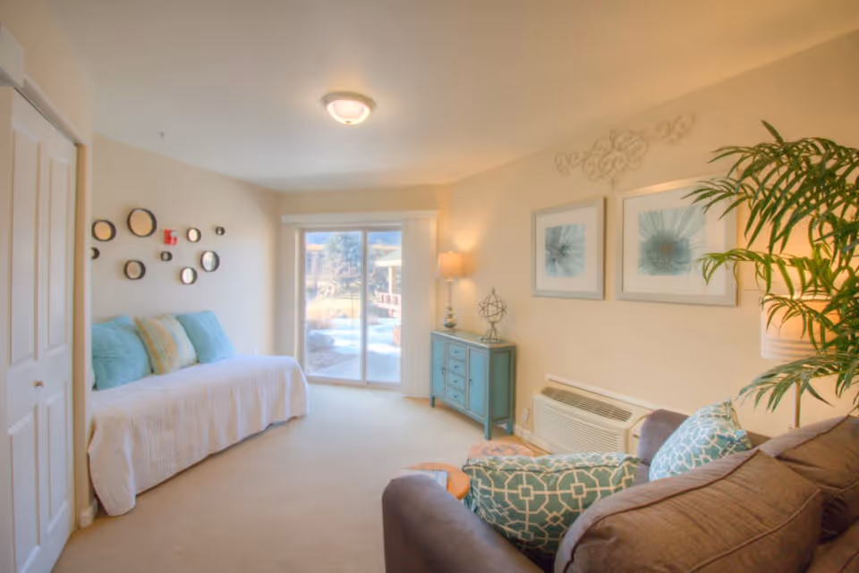 Bright living room with a sofa, daybed, teal cabinet, decorative wall art, and sliding glass doors to the outside.