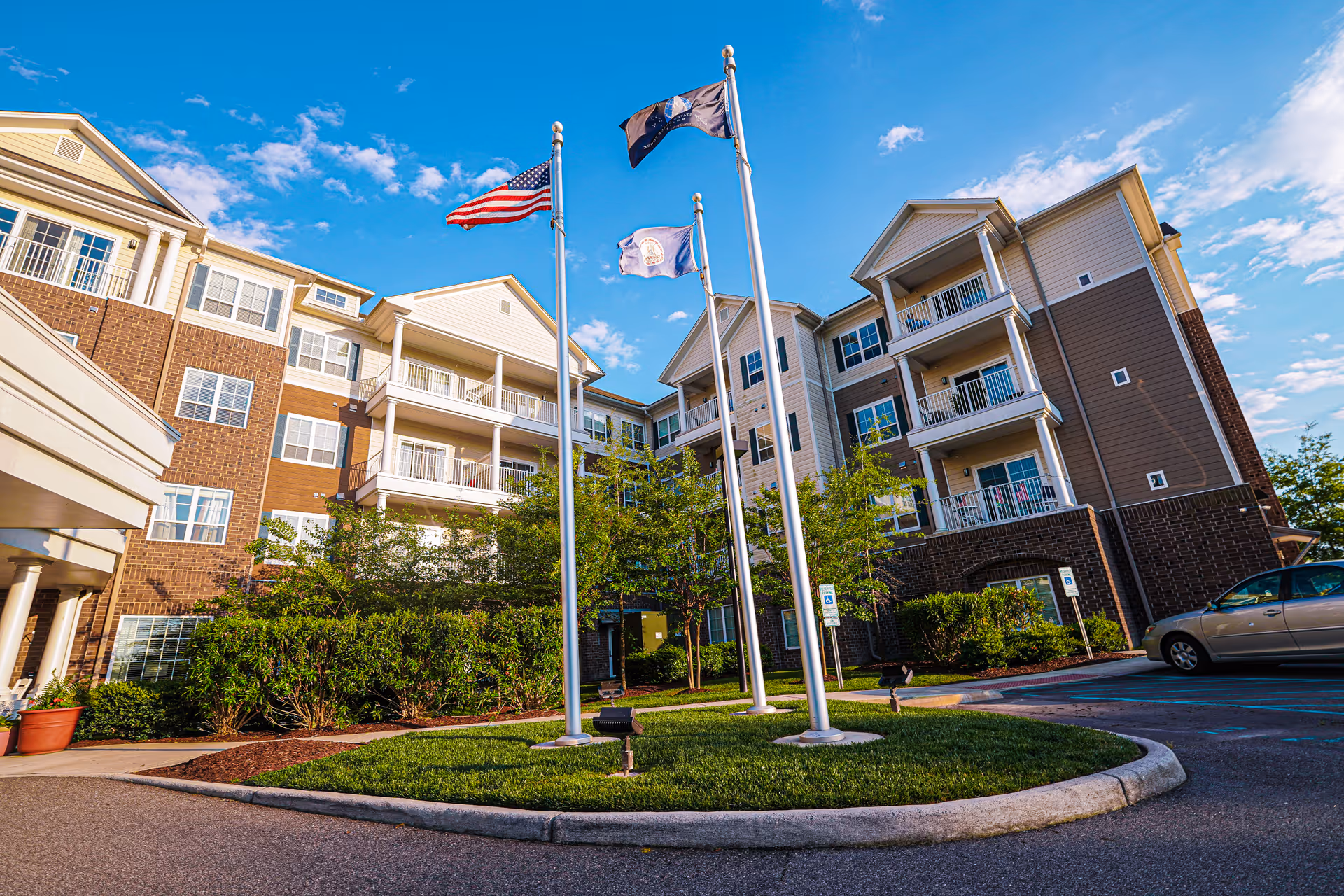 Front exterior of a multi-story senior living building with three flagpoles in a landscaped circular driveway.