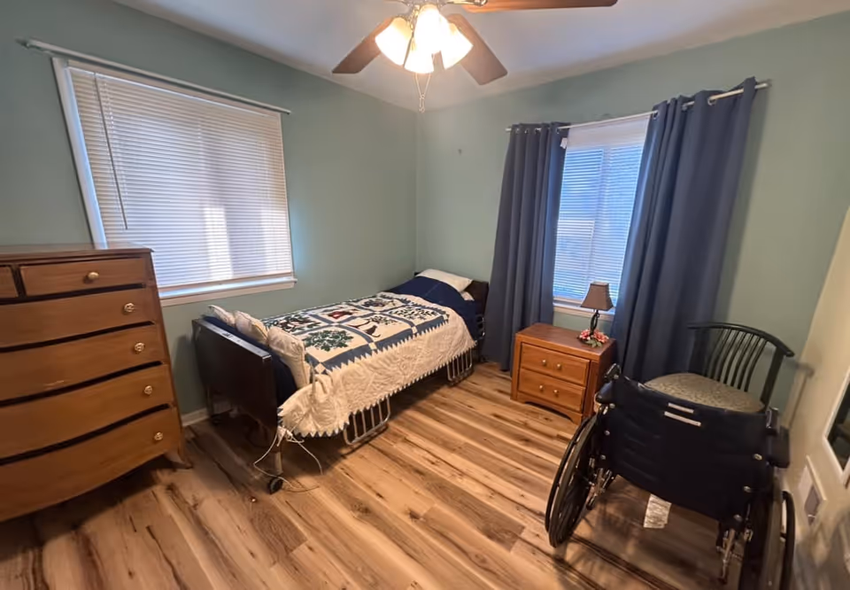 A small bedroom in a senior home with a single bed, dresser, and wheelchair.
