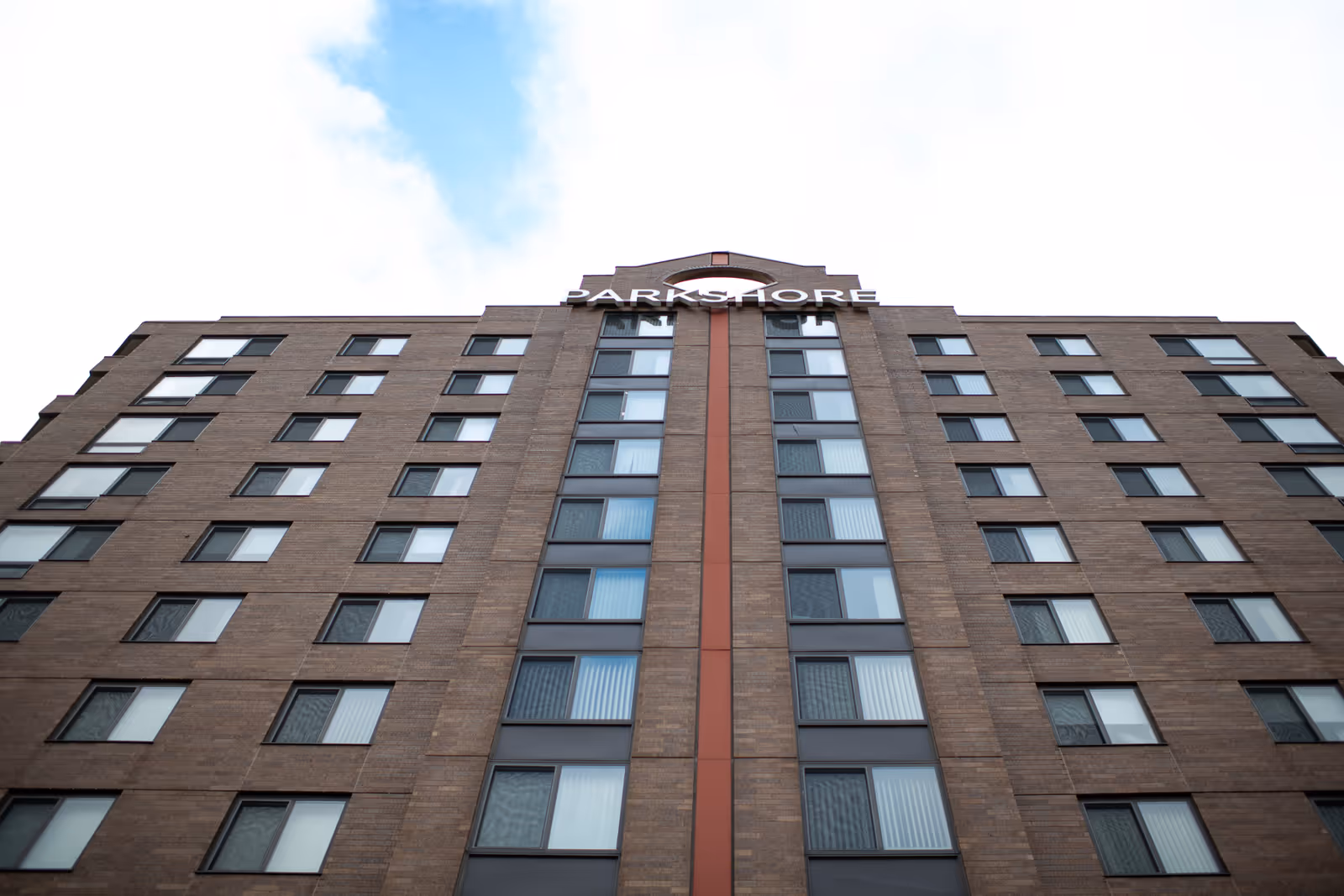 Low-angle view of the Parkshore Senior Campus multi-story brick building facade with rows of windows and a 'PARKSHORE' sign at the top.