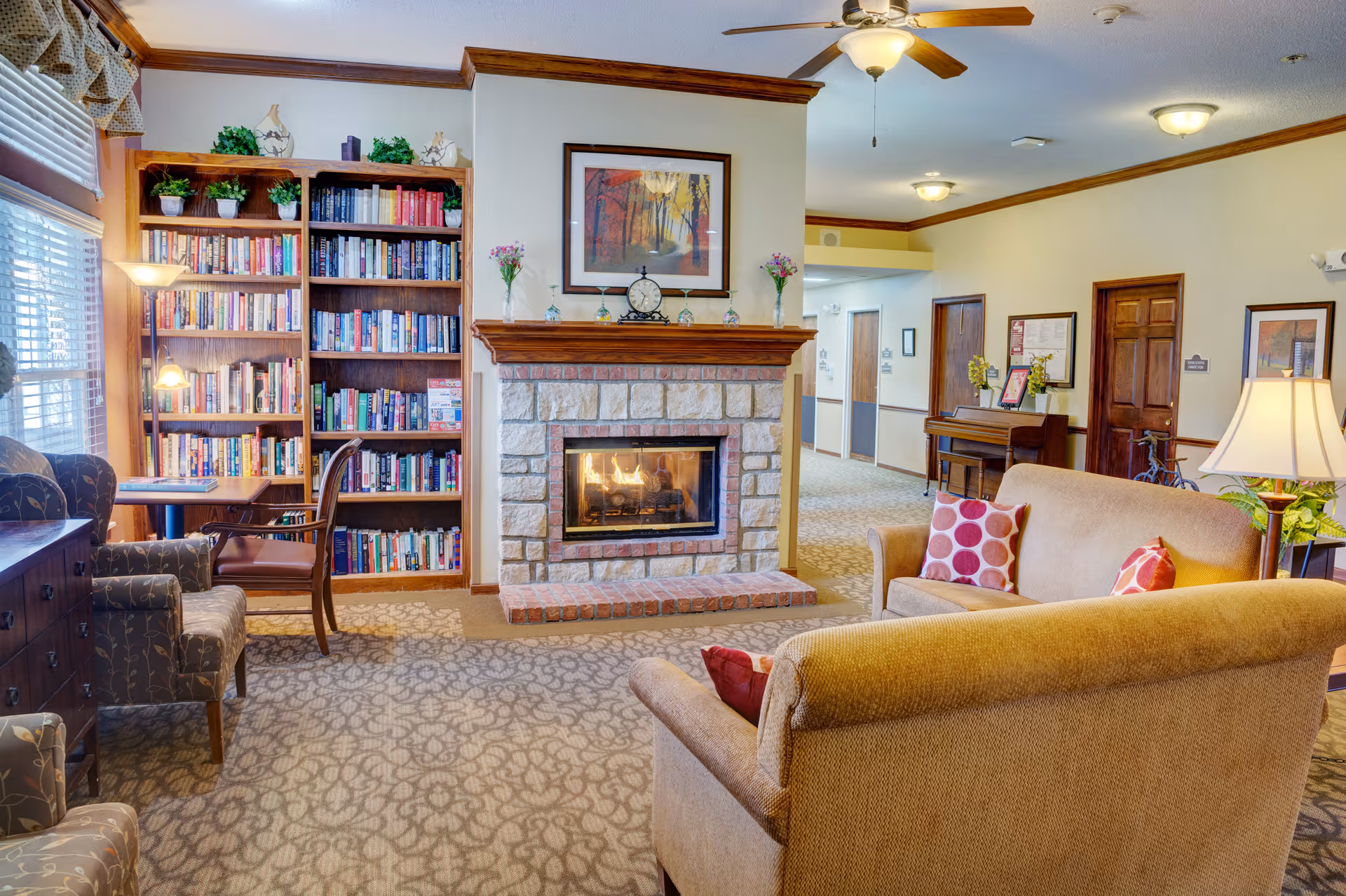 Cozy common room with a stone fireplace, bookshelves, and upholstered seating arranged around a coffee table.