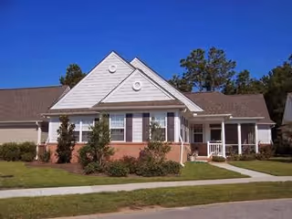 Single-story residential-style building with a front porch, shrubs and lawn under a clear blue sky.