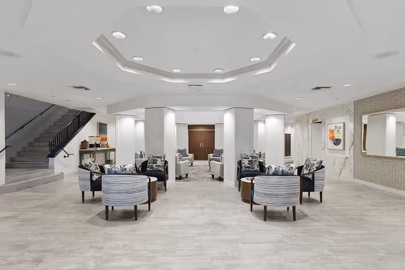 Spacious modern lobby with grouped lounge chairs arranged around small tables under recessed ceiling lighting.