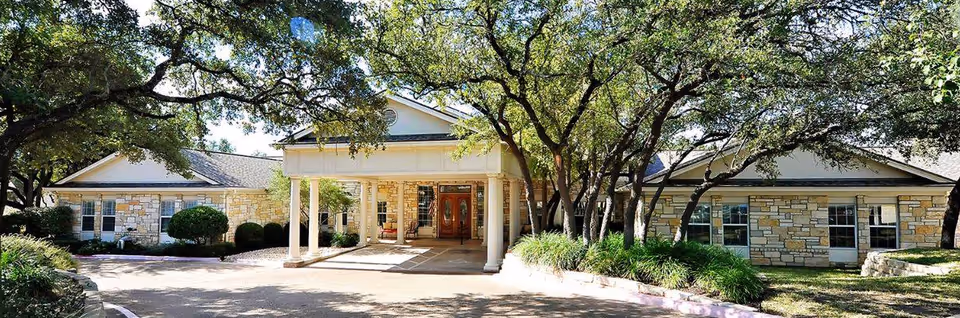 Front view of a stone-clad assisted living facility with a covered entrance and trees.