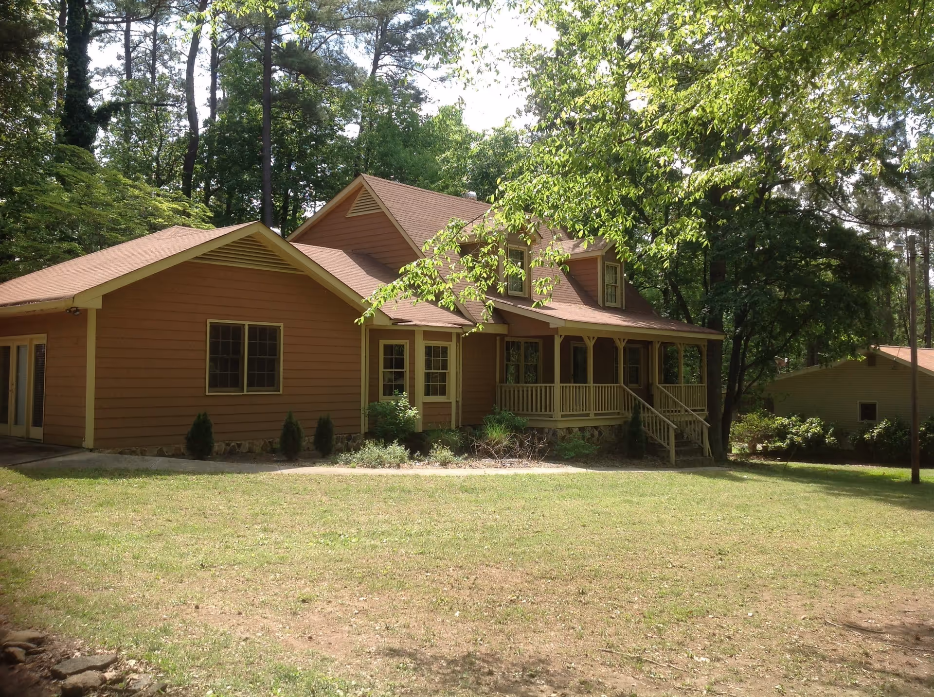Brown single-family house with a covered front porch set among trees and a grassy yard.