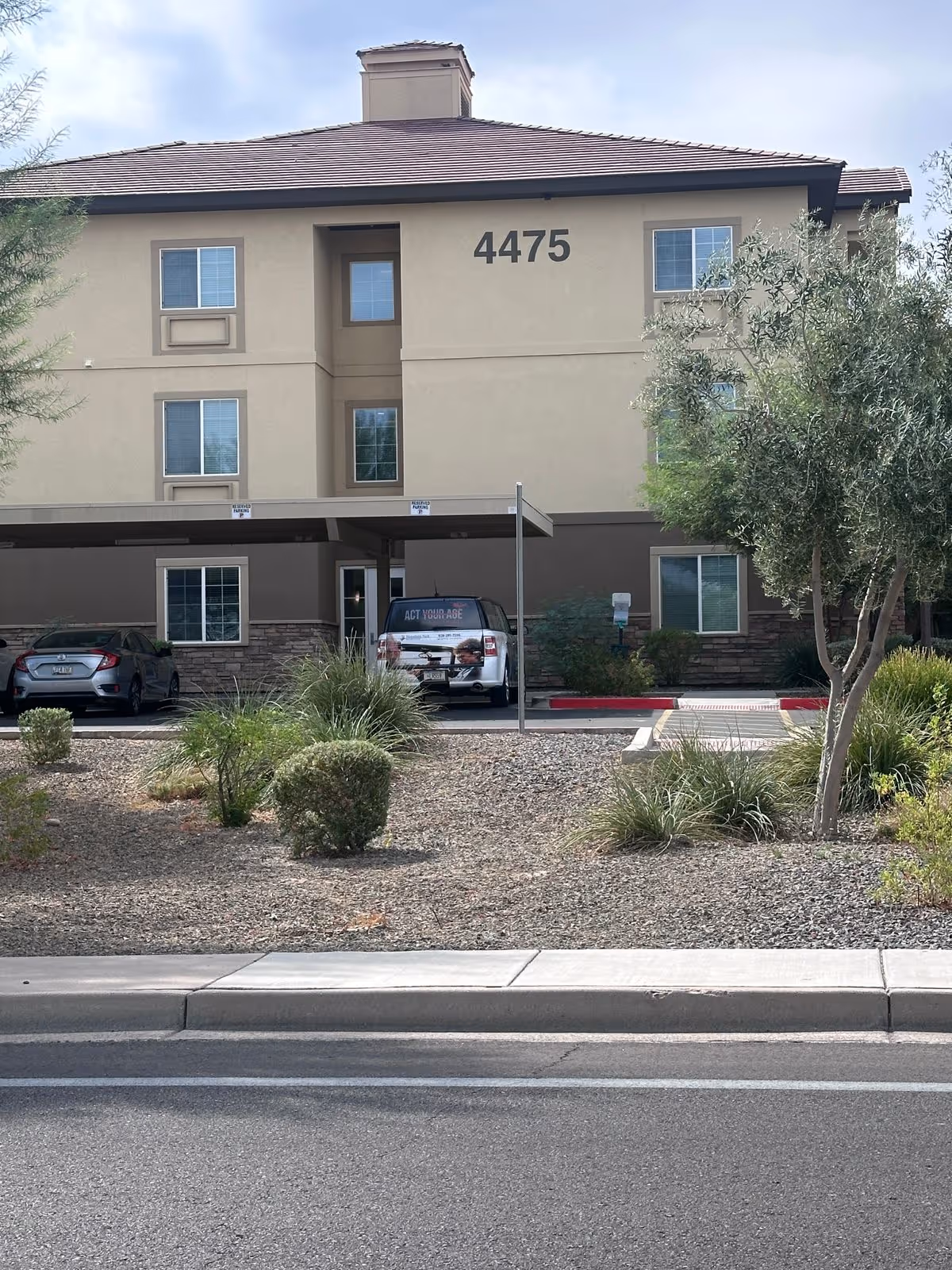Front exterior of a three-story senior living building marked 4475 with covered parking and desert landscaping.