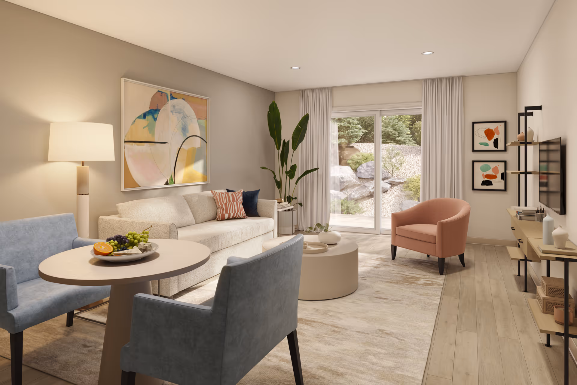 A cozy living room with a beige sofa, two blue armchairs around a small round table with a plate of fruit, a round coffee table, a coral armchair, a TV mounted on the wall, abstract artwork, a tall floor lamp, and large sliding glass doors opening to a garden with rocks and greenery.