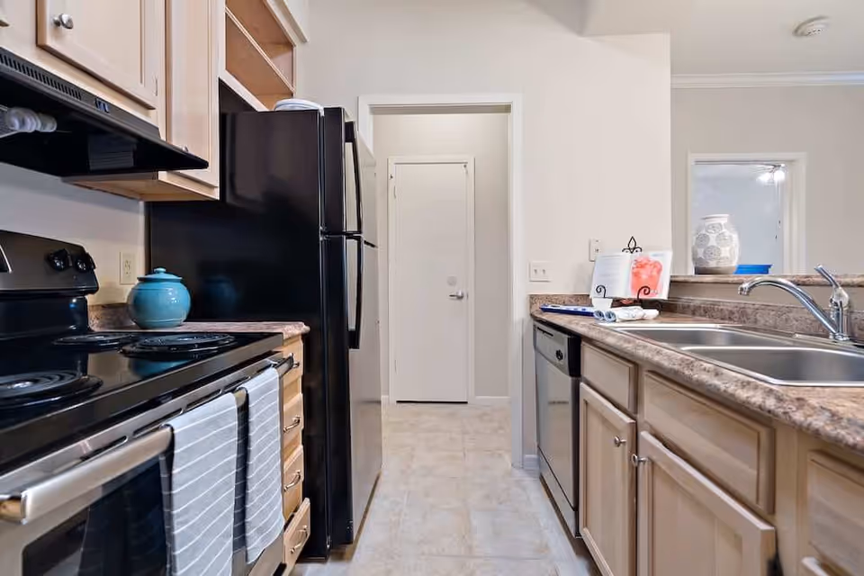Galley-style kitchen with a black refrigerator and stove on the left, a double sink and dishwasher on the right, and a doorway at the far end.