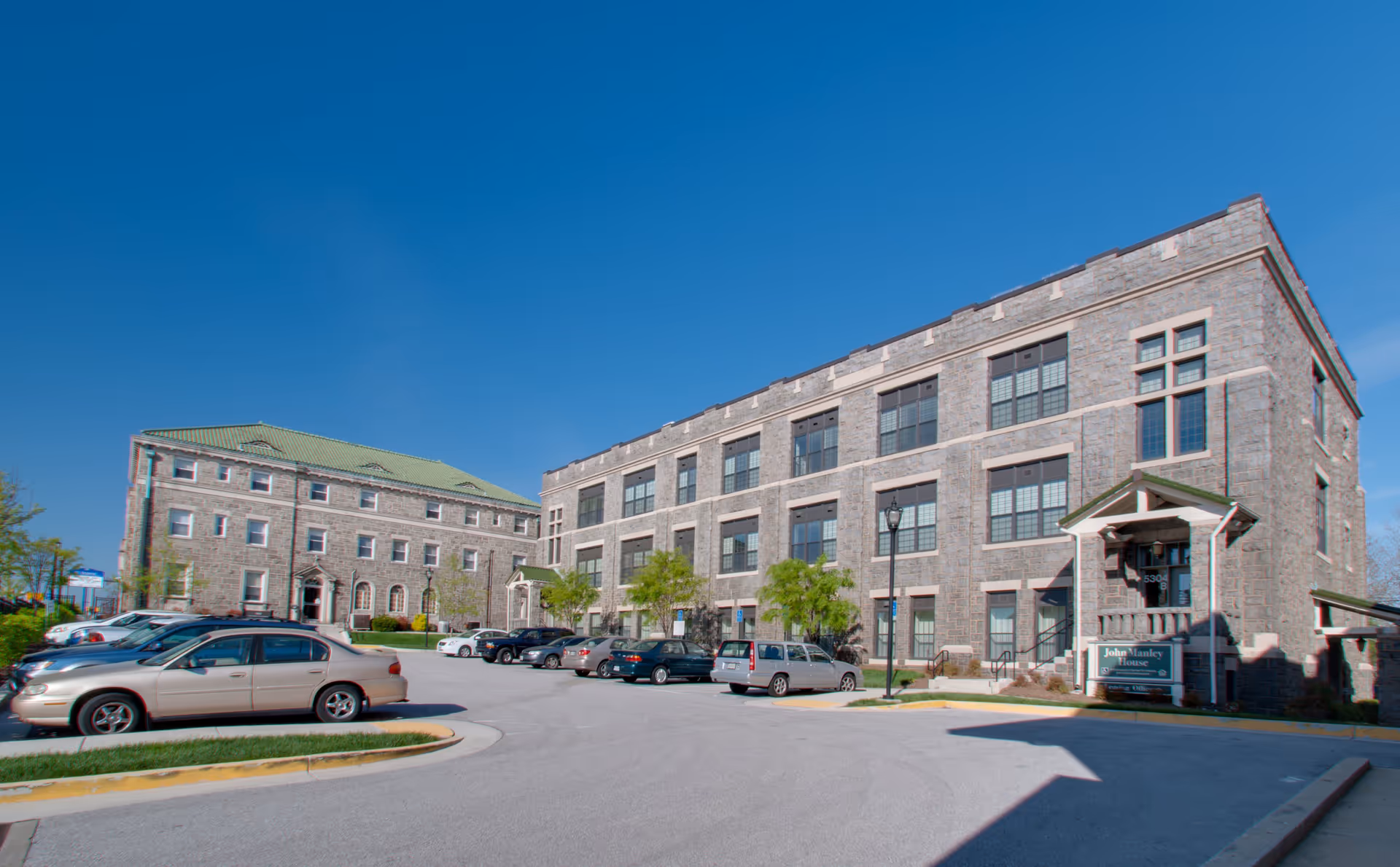 Exterior view of the John Manley House building with a parking lot in front, several parked cars, and clear blue sky above.