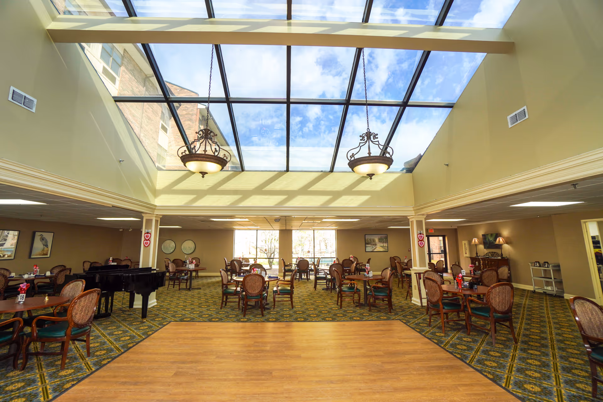 Spacious dining room with a large glass skylight, chandeliers, round tables and chairs.