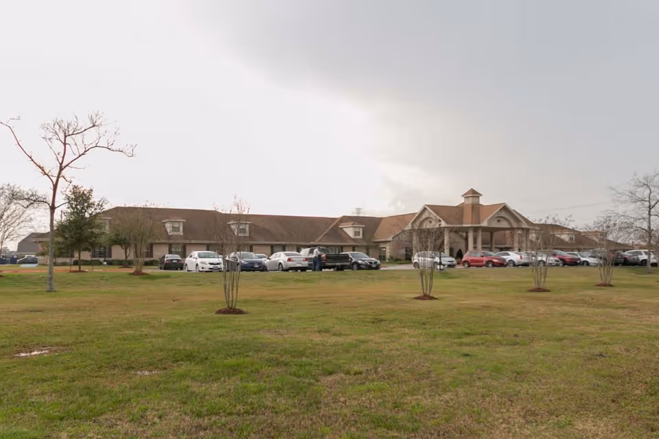 Exterior view of EastView HealthCare & Rehabilitation Center, a single-story building with a pitched roof and a covered entrance. Several cars are parked in front of the building, and there is a grassy area with small trees in the foreground under a cloudy sky.