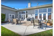 Outdoor patio with several tables and chairs on a concrete terrace in front of large windows and doors of the assisted living building under a clear blue sky.
