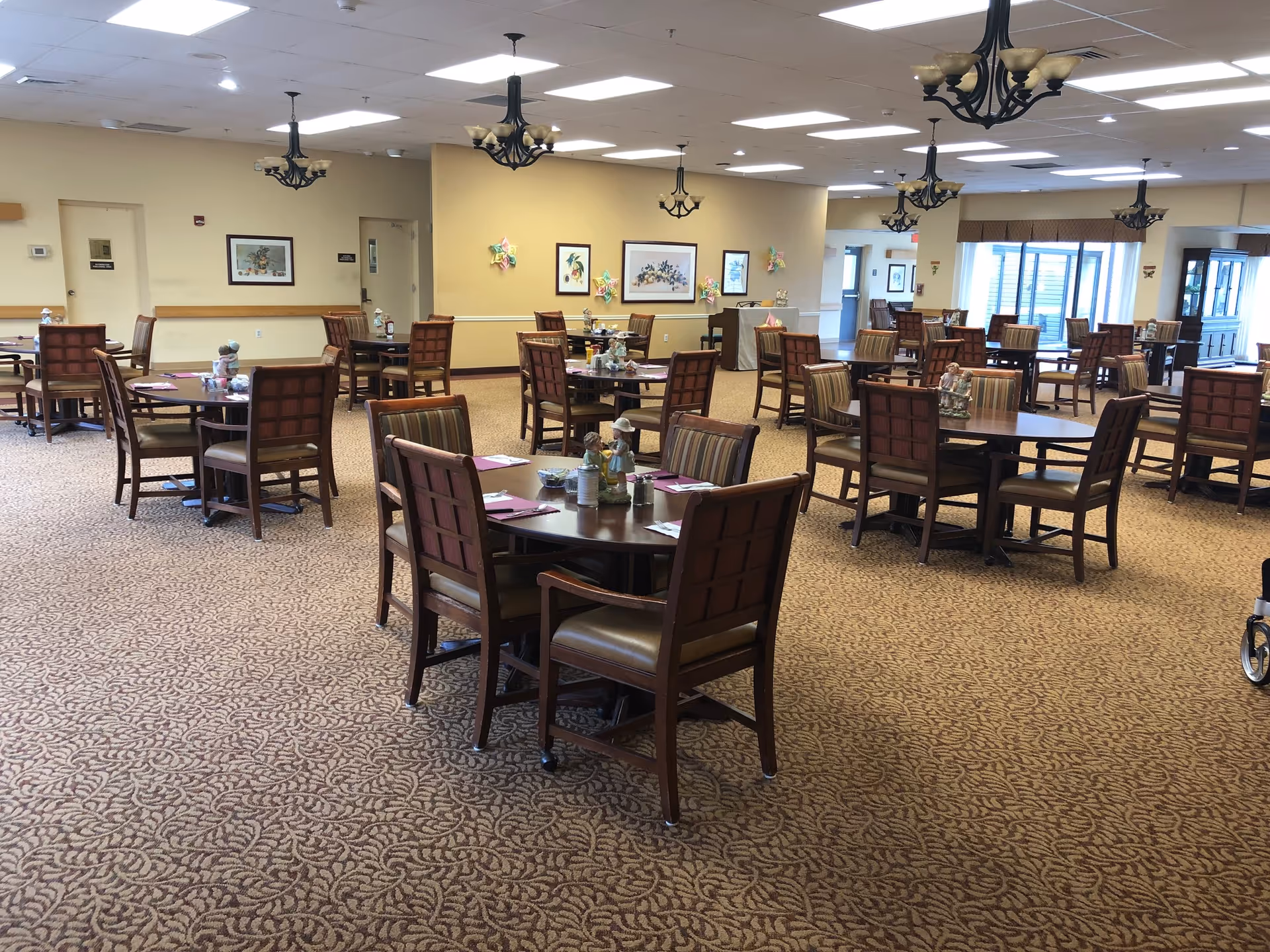 Spacious dining room with multiple round wooden tables and chairs arranged on patterned carpet under chandeliers.