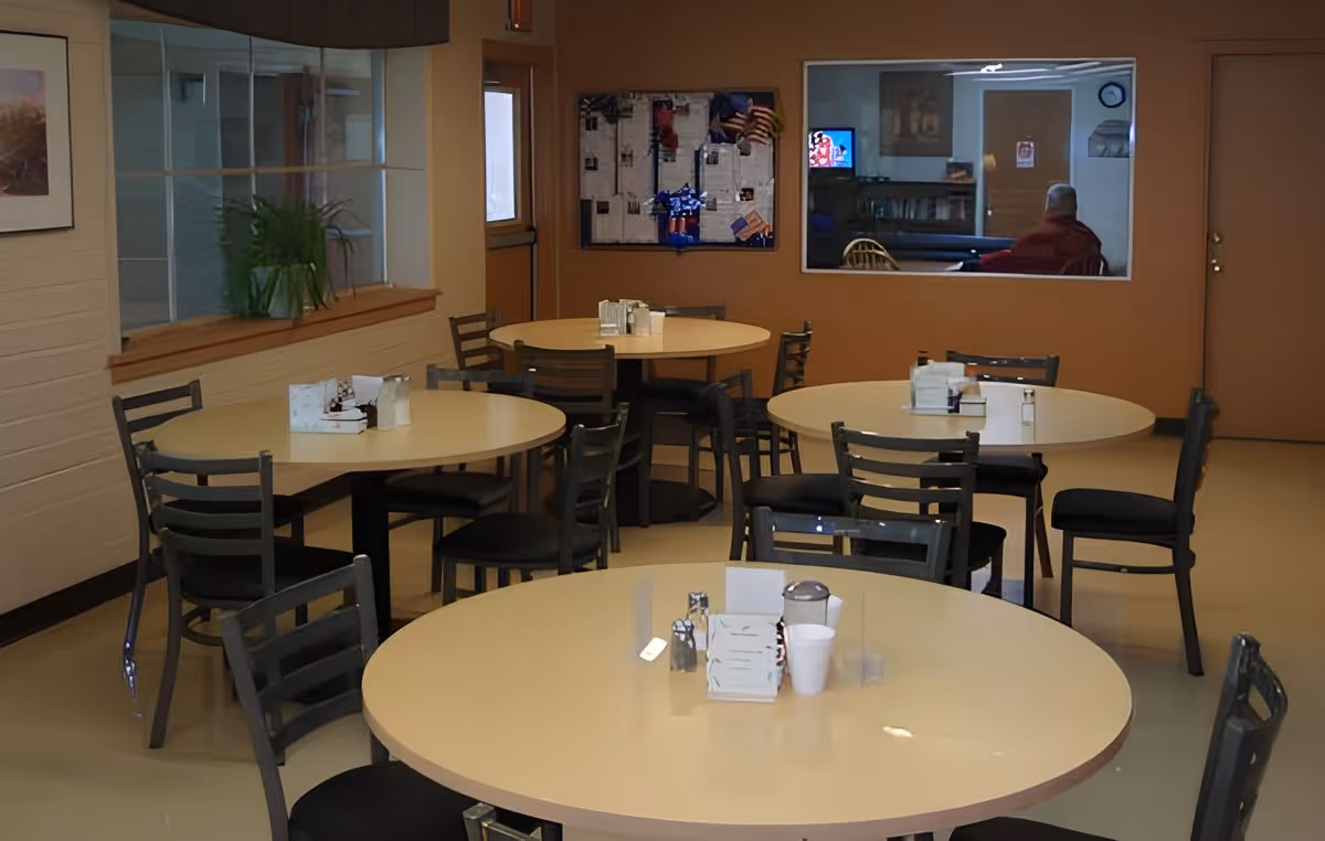 Communal dining room with several round tables and chairs in a senior living facility.
