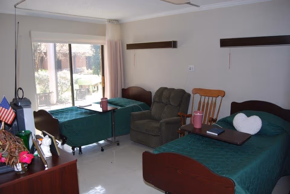 Shared resident bedroom with two single beds, a recliner, and a sliding glass door to an outdoor patio.