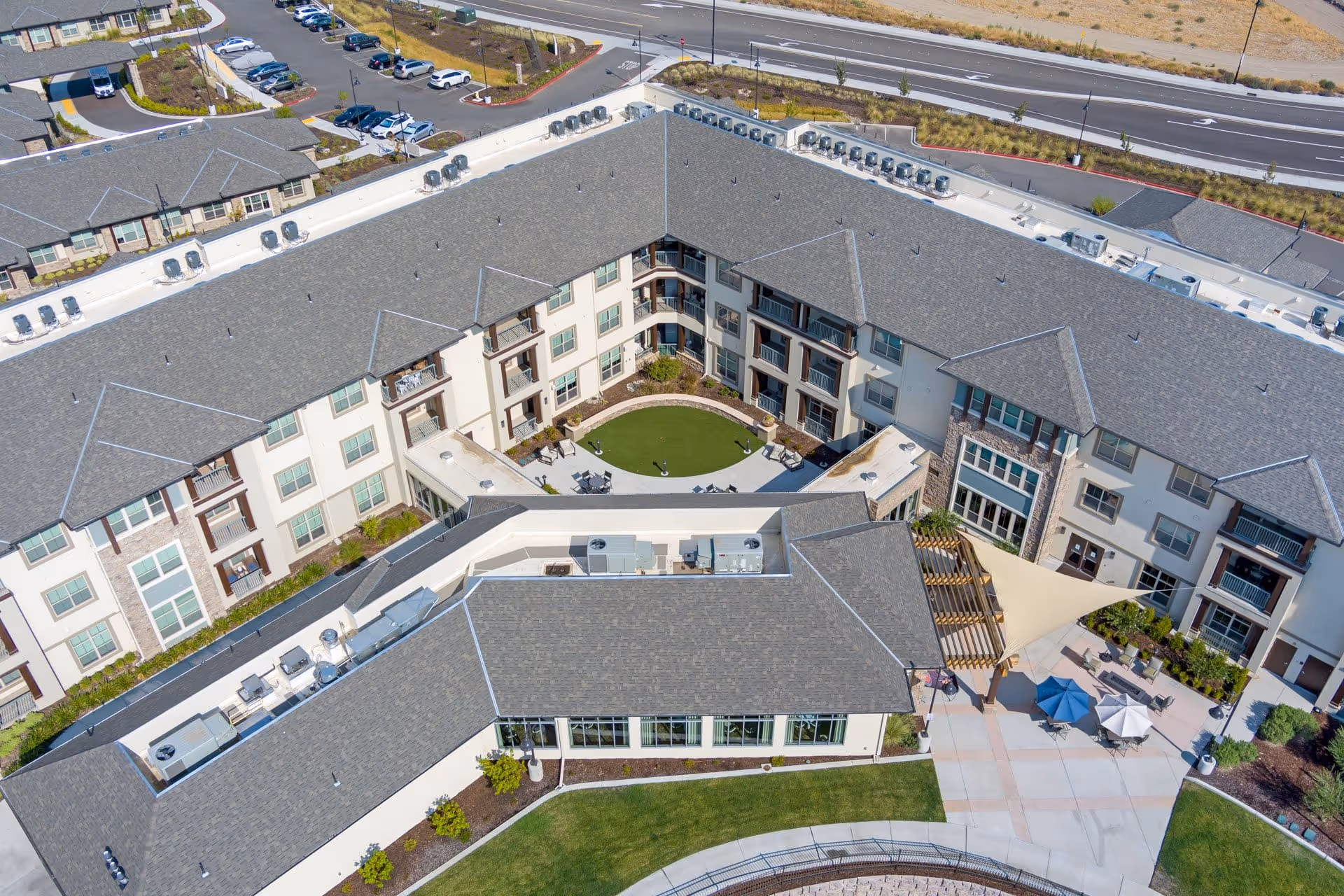 Aerial view of a multi-story senior living building surrounding a central courtyard with a circular lawn, seating areas and umbrellas.
