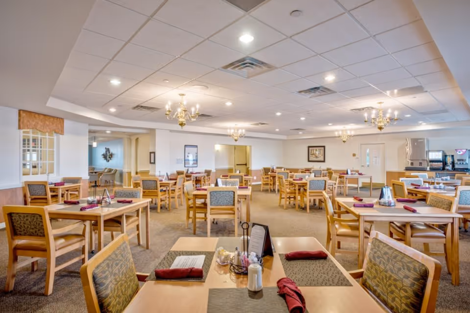 Spacious senior dining room with multiple wooden tables and chairs neatly set with placemats and folded napkins.