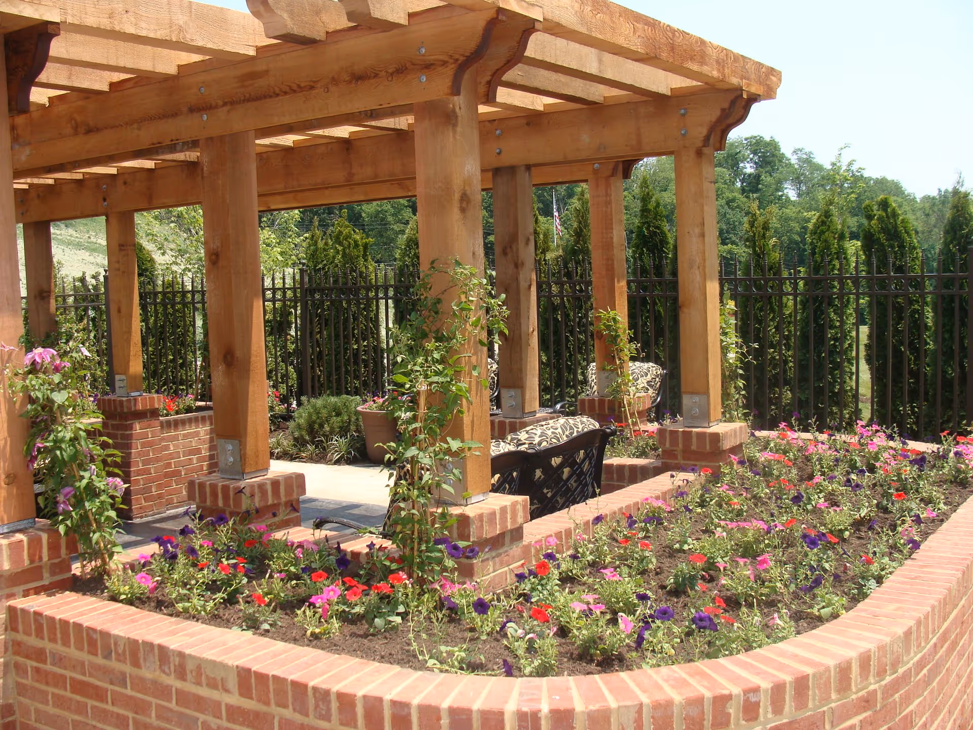 Wooden pergola over a brick planter filled with colorful flowers and outdoor seating.